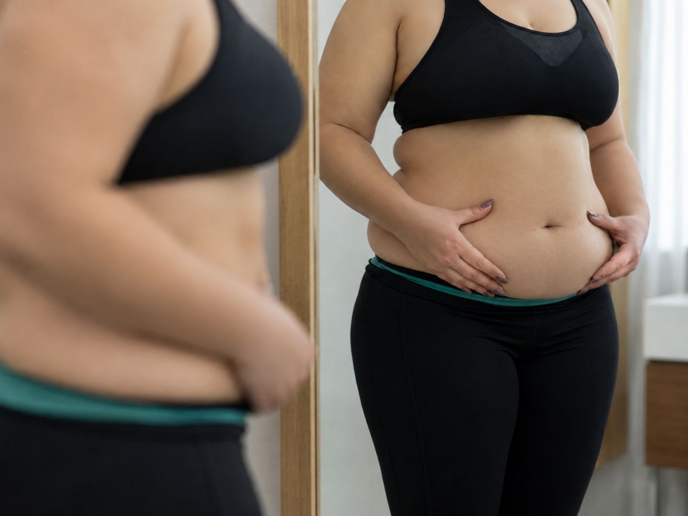 Frau vor dem Spiegel betrachtet ihren Bauch